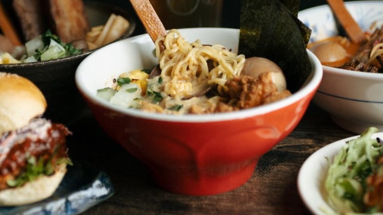 A red bowl of ramen with other dishes around it