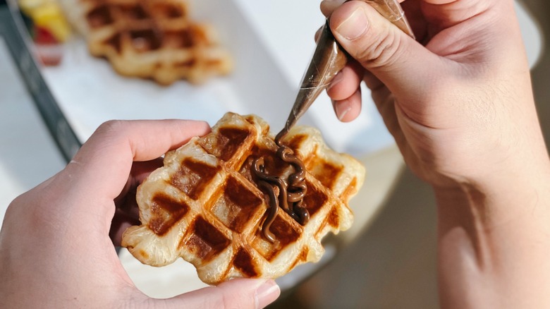 Chocolate sauce being piped onto a croffle