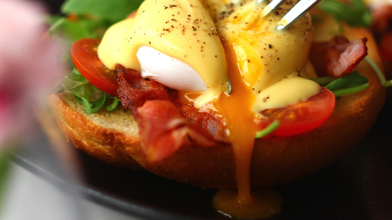 Drippy fried egg yolk pouring out over bacon and tomato on a piece of toast