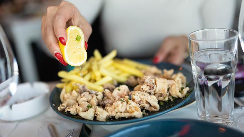 Woman's hand squeezing a lemon over a plate of prepared food to add flavor