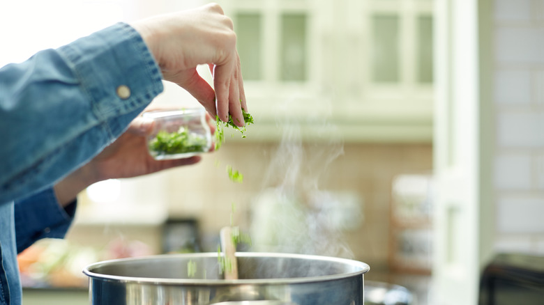 A person sprinkling fresh herbs into a pot on the stove