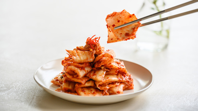 a plate of kimchi made of pickled cabbage with chopsticks picking up a piece