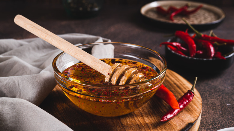 A bowl of hot honey with chili flakes and chili peppers around it