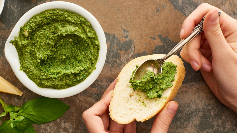 woman adding fresh pesto as a spread on a piece of baguette