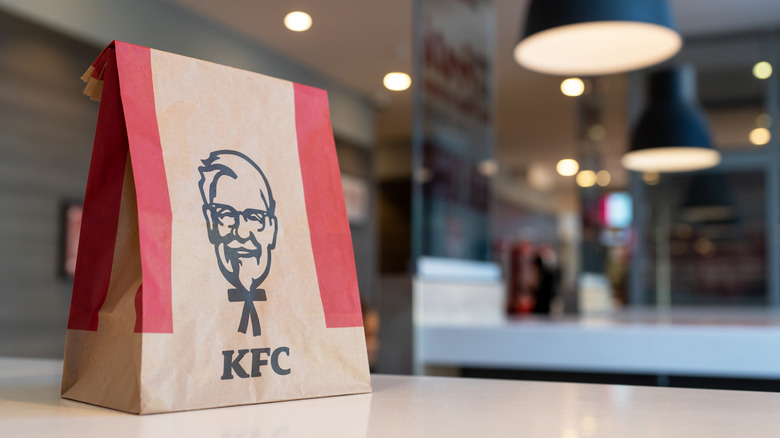 A picture of a KFC bag with the top folded closed sitting on a white table. The background is blurred.