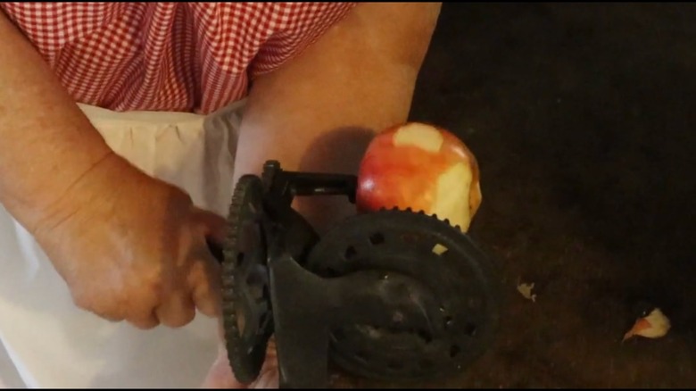 Woman's hands shown using an old fashioned apple peeler while peeling an apple