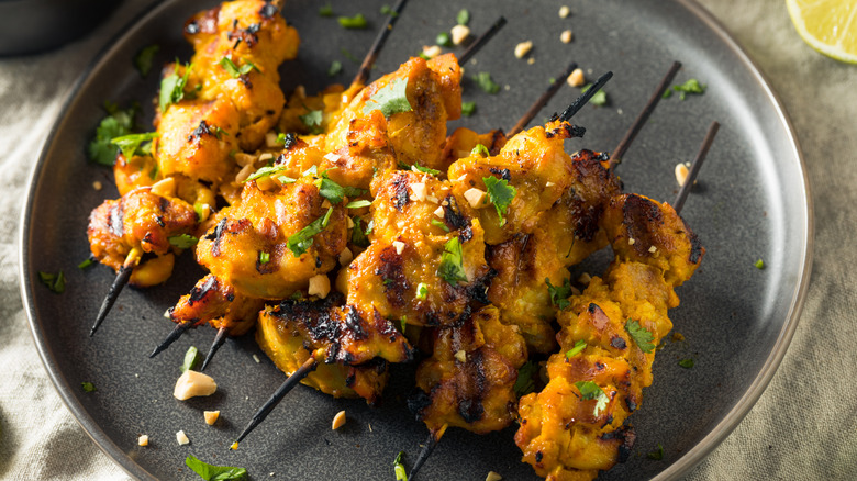 Several chicken satay skewers piled on a dark plate
