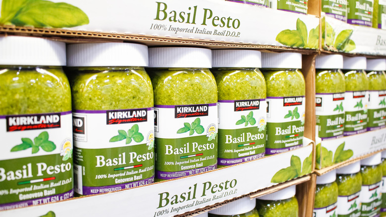 A supermarket shelf lined with jars of green Kirkland pesto