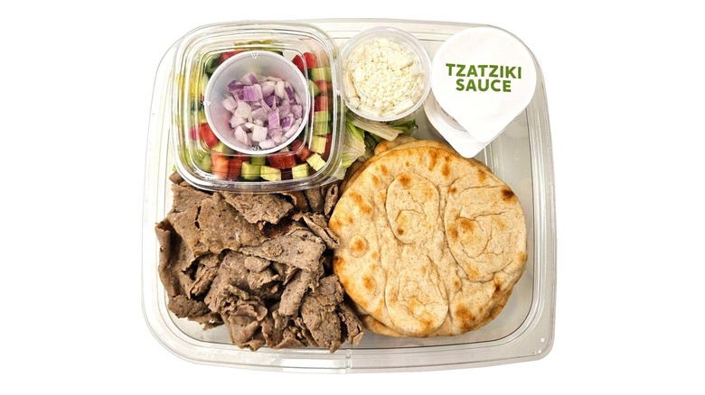 A plastic box containing pita bread, shaved meat, tzatziki sauce pots, and separately packaged vegetables and feta cheese