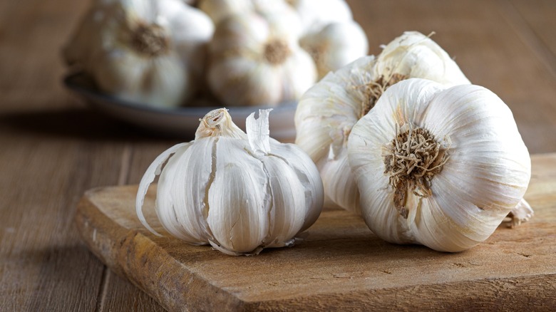 Group of fresh organic garlic bulbs on wooden cutting board.