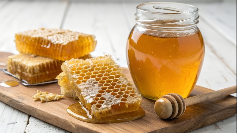 Fresh honeycomb and golden honey jar on wooden board