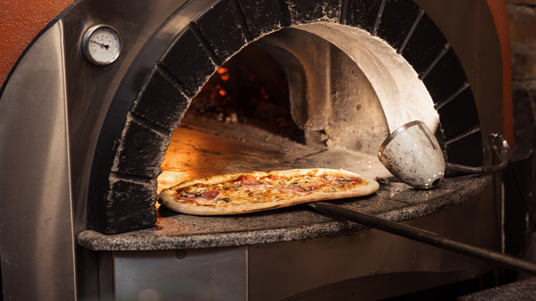 A pizza is being removed from a pizza oven with a pizza peel.