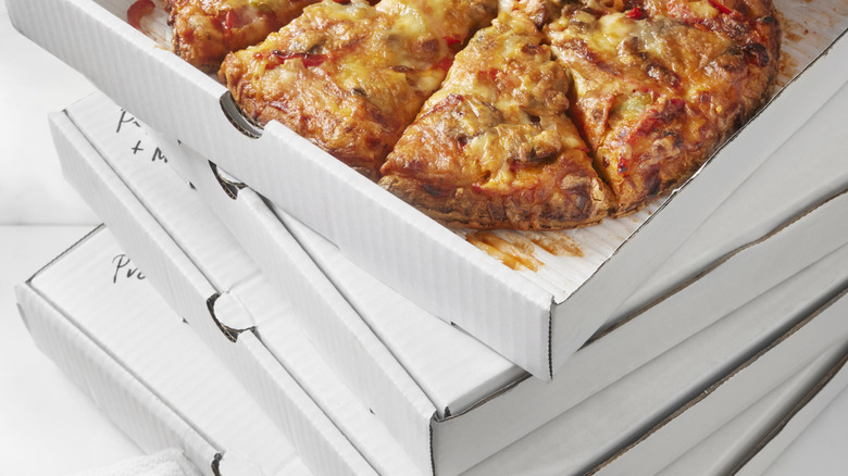 A stack of white pizza boxes, with the one on top opened. A pizza is inside the box.