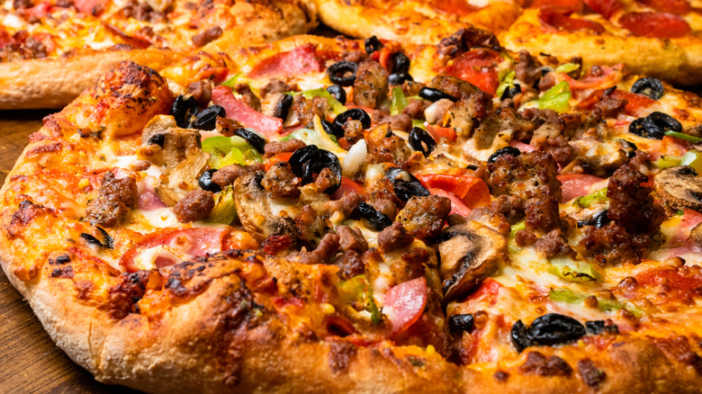 A pizza loaded with many different types of toppings including mushrooms, bacon, peppers, olives, and pepperoni.