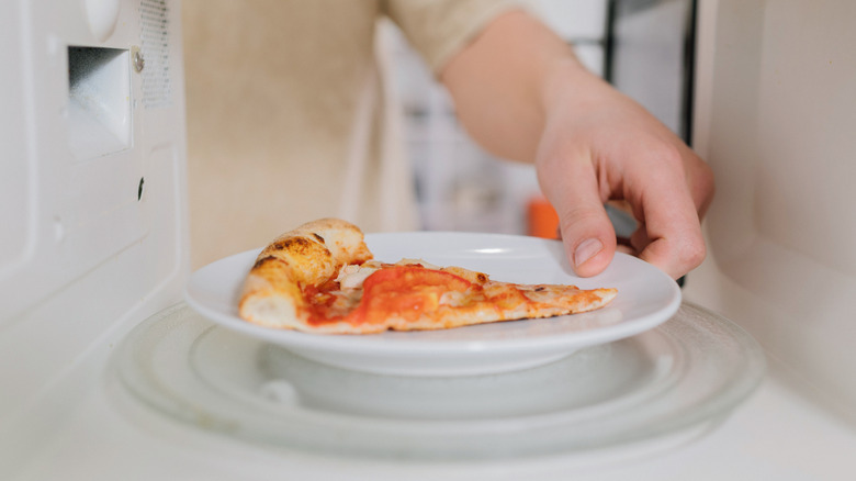 A piece of pizza is being placed into the microwave on a white plate.