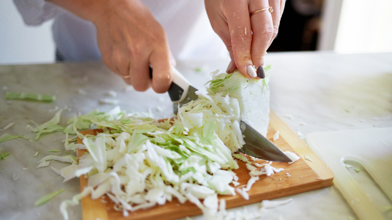Woman's hands and knife cutting cabbage
