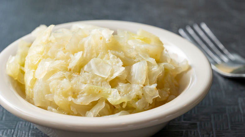 Close up of steamed cabbage in white bowl with fork