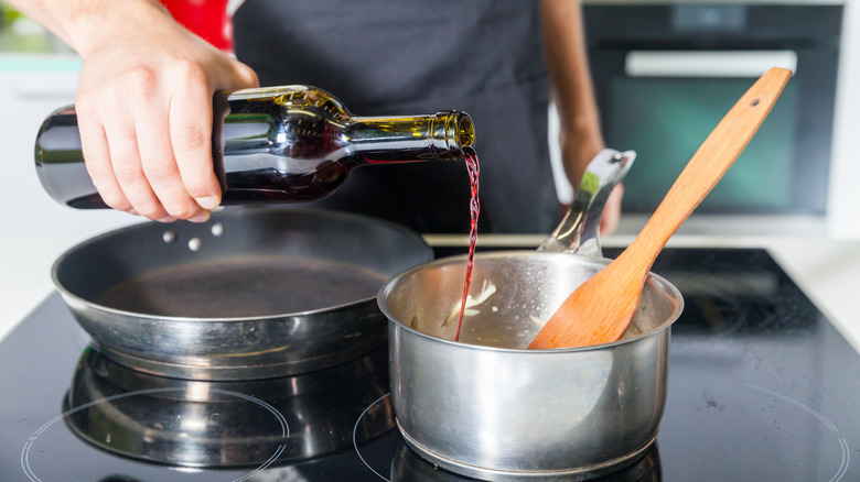 Close-up of a bottle of red wine being poured into a pot on the stove