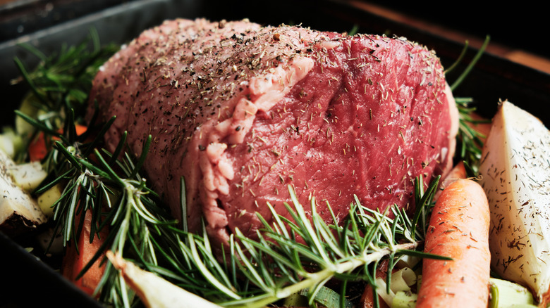 Raw seasoned roast surrounded by fresh herbs