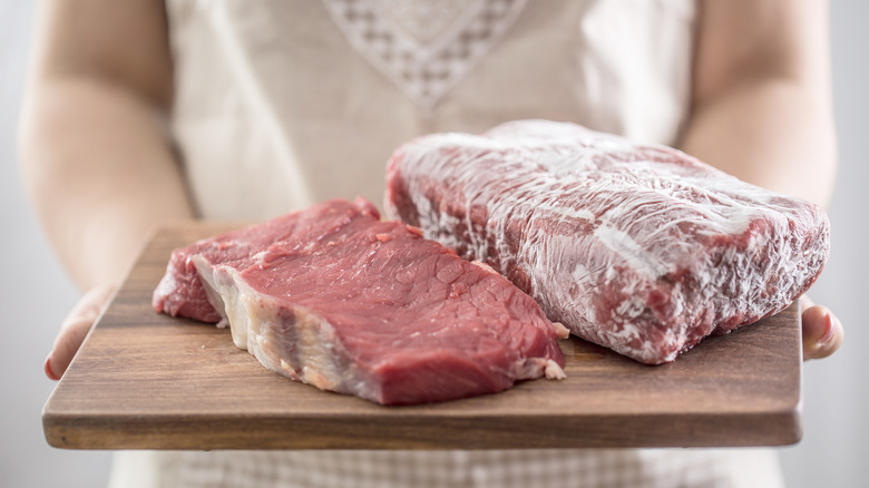 A person holding frozen steak on a wood cutting board