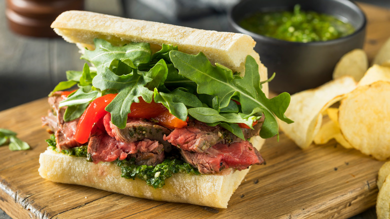 Steak sandwich topped with arugula, peppers, and chimichurri