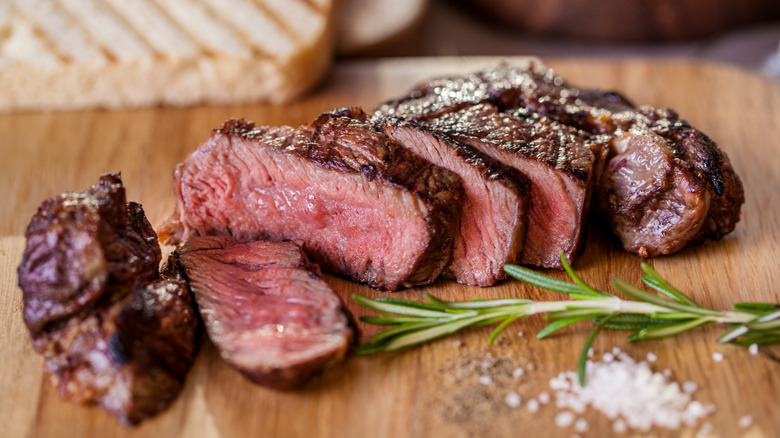 Grilled steak slices on a wood board with fresh herbs