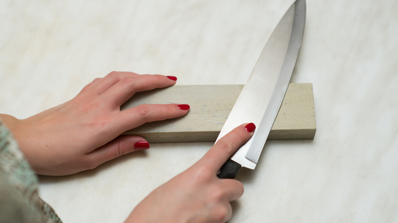 Hands sharpening a knife blade on a stone