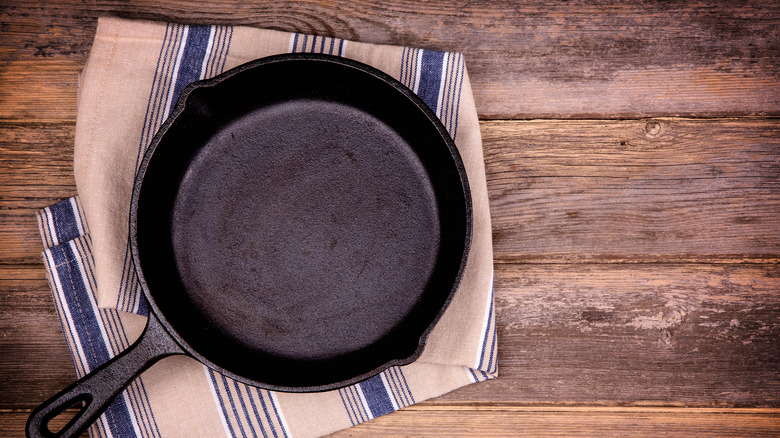 Empty cast iron skillet on towel on wooden table