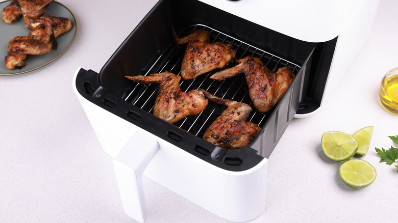 chicken wings in air fryer and on plate on white surface