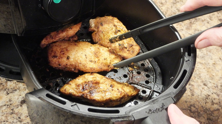 person flipping chicken in air fryer