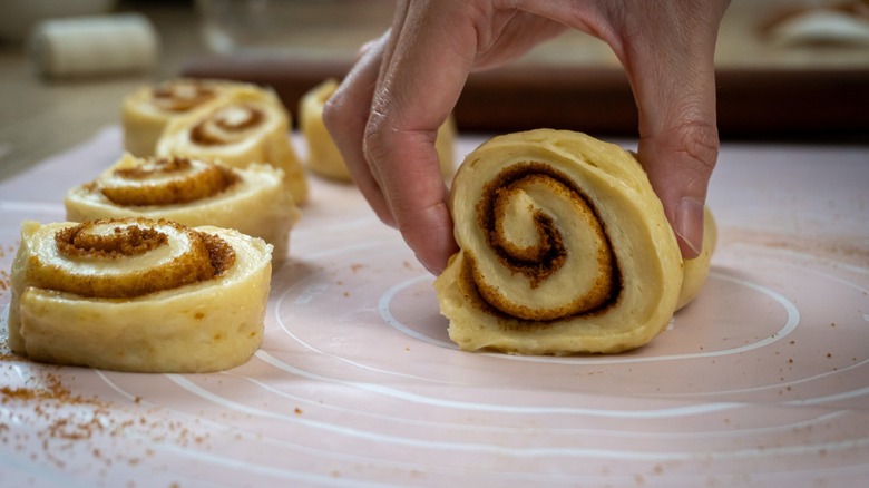A hand pinching a cinnamon roll, ready for baking.