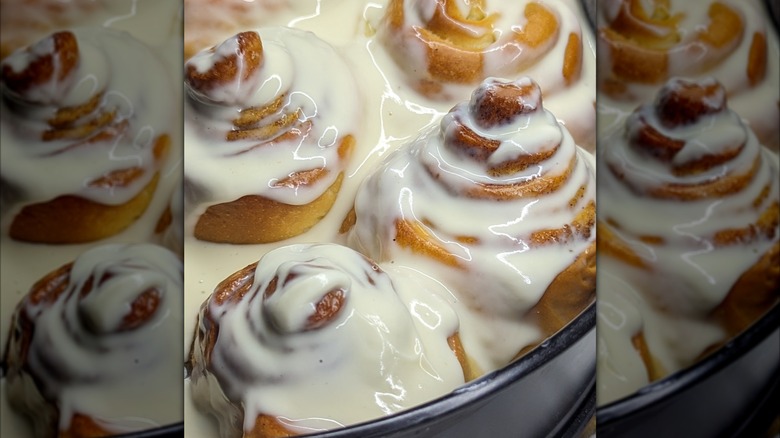 A tray of hot cinnamon rolls, covered in melted frosting.