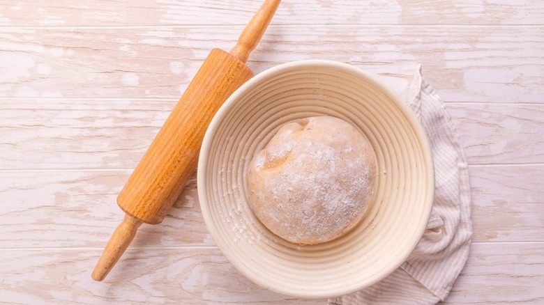 A ball of rising dough in a bowl, next to a rolling pin.