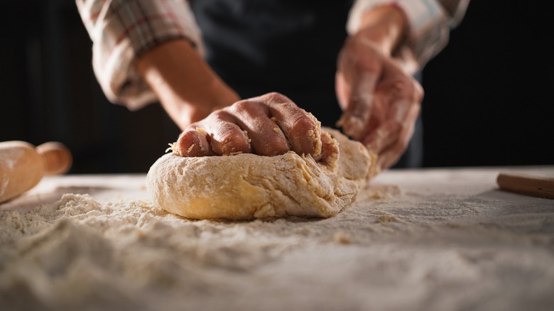 Hands kneading a ball of dough on a floured surface.