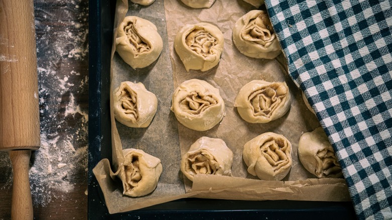Uncooked cinnamon rolls proofing, covered by a kitchen cloth.
