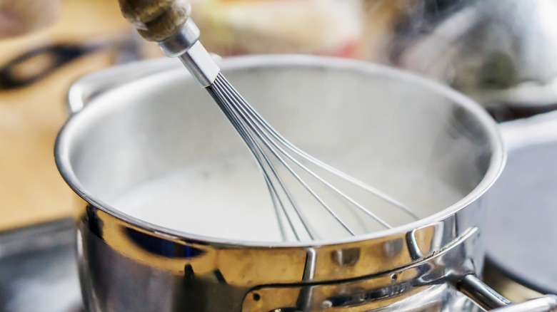 Milk being heated in a saucepan and a whisk