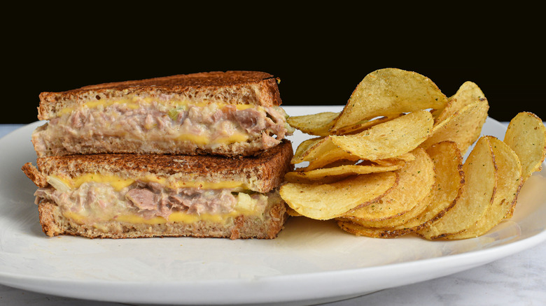 Tuna melt cut in half with chips on a white plate