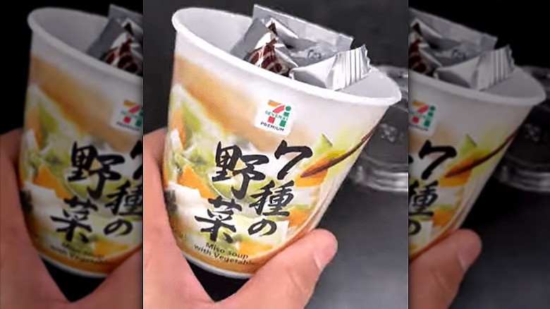 A hand holding Japan 7-Eleven miso soup with vegetables.