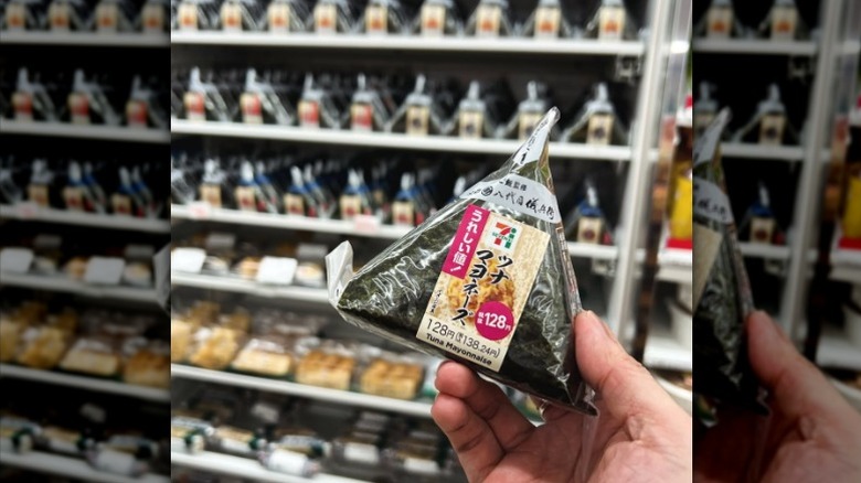 A hand holding a tuna mayonnaise onigiri from a Japanese 7-Eleven.