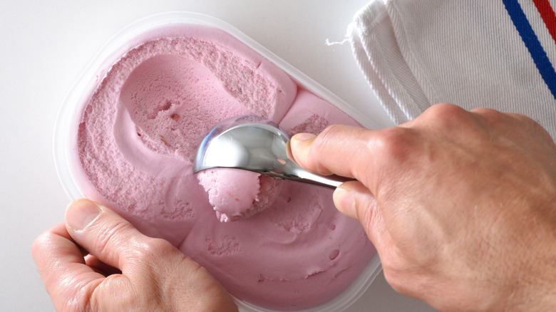hand scooping pinkish-mauve ice cream out of a carton