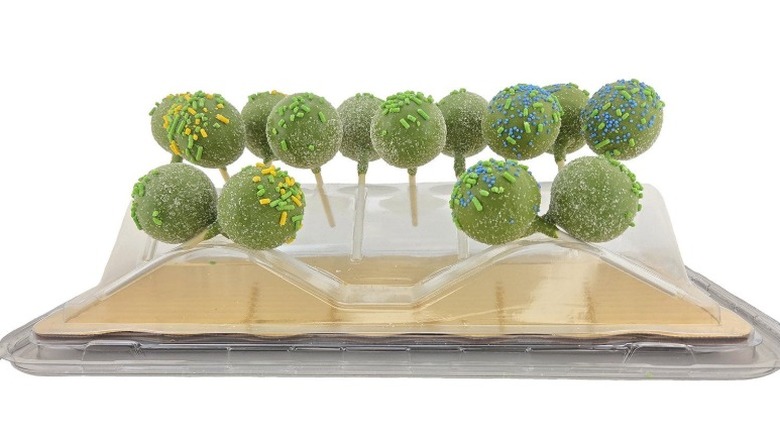 Green-colored cake pops with sprinkles in clear plastic packaging over a cardboard tray