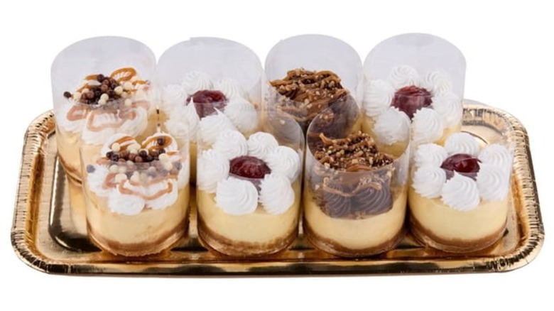 Eight small cheesecakes in clear plastic cylinders sitting on a bronze-colored foil tray