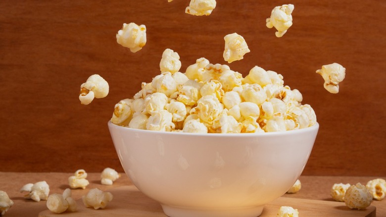 Front view of Popcorn falling into white bowl on wooden background. Minimalist product concept