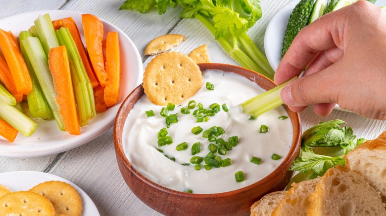 Cottage cheese high-protein ranch dip with fresh vegetables, bread and crackers on wooden white table copy space. Eating diet healthy curd cheese spread with various snacks