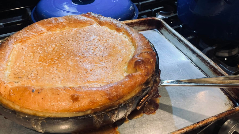 A chicken pot pie made from pizza dough rests inside of a pan, on top of a baking sheet.