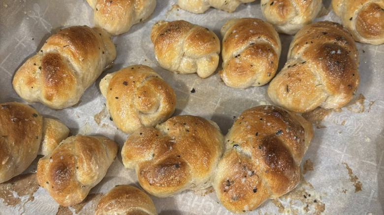Several garlic knots on a pan lined with baking paper, sprinkled with spices.