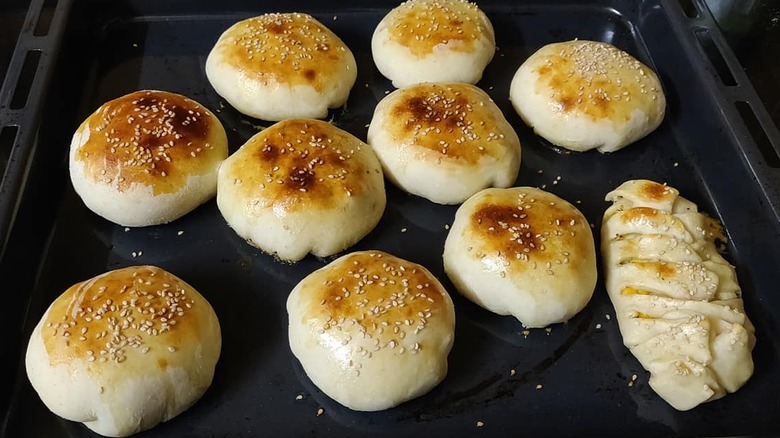 Several stuffed chicken buns rest in a pan, sprinkled with sesame seeds.