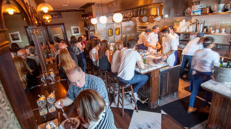 Busy and tiny interior dining area filled with diners and chefs preparing in an open kitchen at Petit Trois in Los Angeles