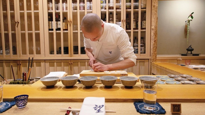 Chef TJ preparing food behind the chef's counter at Sushi Noz in New York City