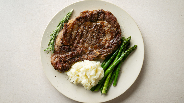 A cooked ribeye steak served with mashed potatoes and asparagus.